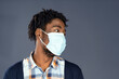 © Svyatoslav Lypynskyy - Dark-skinned Guy with Dreadlocks on his Head in a Medical Mask Looks to the Copy Space on a Gray Background. Social Distance, Self-isolation, Pandemic, Quarantine. Close-up