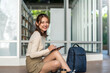 © amnaj - Young Asian female student sitting holding book looking at camera. Library background