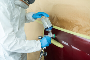 Wall Mural - Close up view of auto painter in a protective suit and mask sprays a degreaser or other cleaner on a car door using a spray gun. Preparation of vehicle body elements for local repair