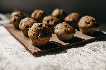 Homemade muffins with blueberries on brown wooden board on white table, boho napkin, leaves, sunlight. Tasty cakes, sweets, cupcakes. No sugar, free gluten. Receipt. Sweet dessert buffet. Mother’s day