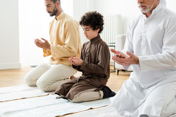 Wall Mural - Preteen arabian boy praying near men at home.