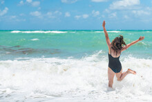 Back Of Young Woman In Swimsuit Jumping Running To Green Turquoise Water In Sunny Isles, Miami Beach, Florida With Atlantic Ocean Sea And Sargassum Seaweed