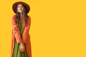 Wall Mural - Young fashionable woman wearing felt hat on yellow background