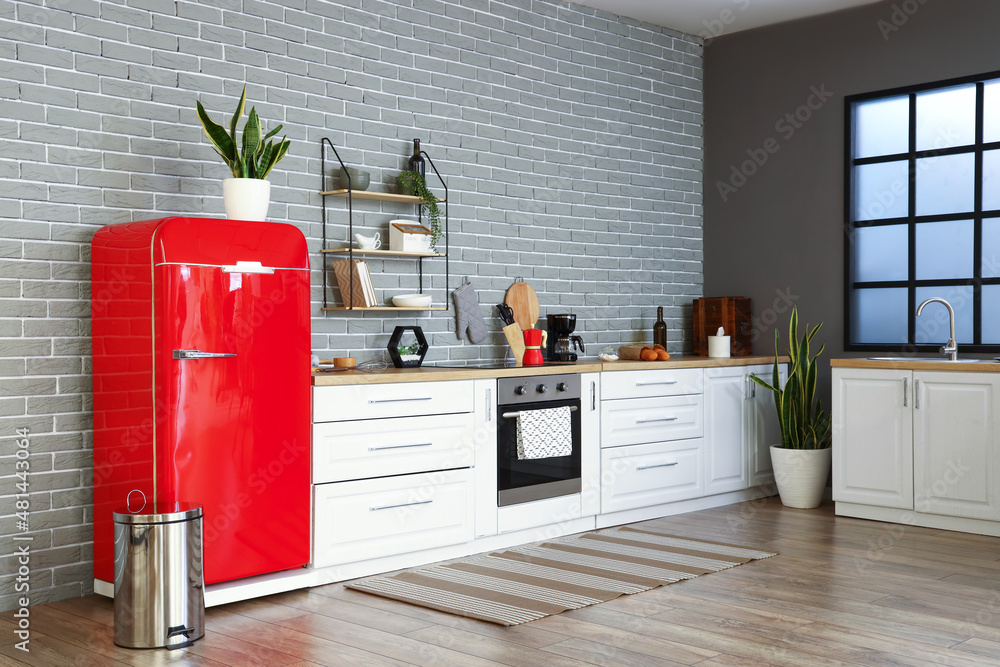 Interior of stylish kitchen with red fridge, white counters and brick wall