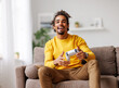 © JenkoAtaman - Young positive happy african american guy with wireless gamepad playing video game at home