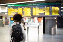 Young Male Traveler Looking At Departures And Arrivals Panel At Airport Or Train Station. Space For Text.