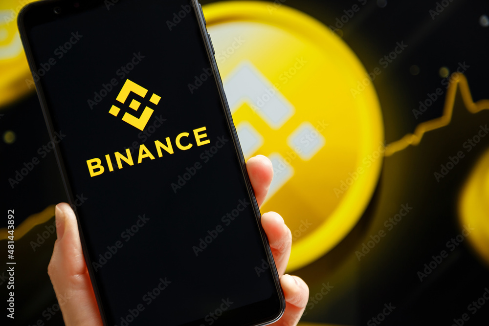 Ukraine, Odessa - October, 9 2021: Hand holding mobile with Binance app running at smartphone screen with Binance logo at background. Binance is cryptocurrency exchange and trading platform