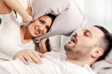 Wall Mural - A woman with pillow covering her ears because of her husband's snoring.