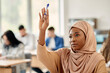 Muslim university student raises her hand to answer question while attending a class at lecture hall.