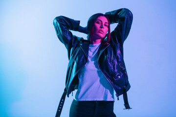 Pretty young stylish girl model in fashionable outerwear with white t-shirt and black leather jacket in studio with pink and blue light