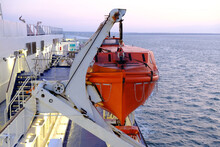 Red Lifeboat Hangs On Ferry. White Deck Of Large Passenger Ferry.  Lights On Deck In Morning. 