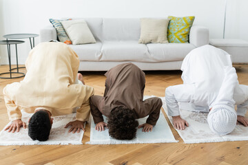 Canvas Print - Arabian men and boy bending on rugs while praying at home.