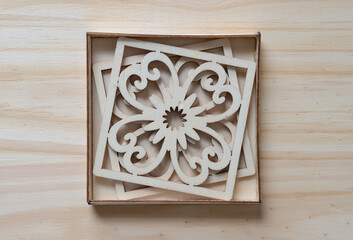 two decorative square ornaments inside a shallow wooden box on a wooden surface