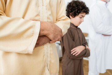 Canvas Print - Young muslim man praying near blurred son at home.