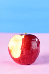 beautiful red apples seen from the side isolated on pink and blue background, bitten apple