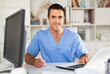 © JackF - Portrait of smiling experienced physician filling up medical forms on laptop while sitting at table in office