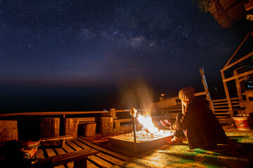 Wall Mural - female traveler sitting near campfire under night sky with stars and milky way. night camping. hikin