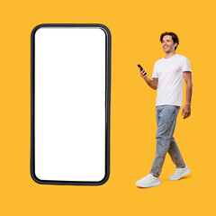 Wall Mural - Young bearded man walking with cellphone isolated on yellow wall