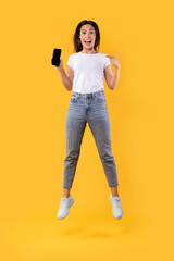 Wall Mural - Woman showing white empty smartphone screen and jumping up