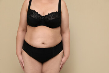 Wall Mural - Beautiful overweight woman in black underwear on beige background, closeup with space for text. Plus-size model