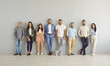 © Studio Romantic - Ready to make success happen. Team of happy successful and modern business people standing leaning against gray wall in empty office. Variety of men and women stand in row and look at camera.