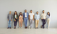 Ready To Make Success Happen. Team Of Happy Successful And Modern Business People Standing Leaning Against Gray Wall In Empty Office. Variety Of Men And Women Stand In Row And Look At Camera.