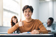 © Prostock-studio - Asian male student sitting at desk showing thumbs up gesture