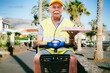 © Manpeppe - A senior delivery man smiling and selling pizzas as he's ready to drive away on his scooter. Job and pensioner concept.