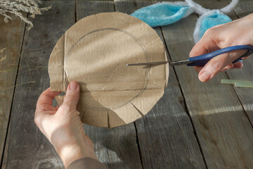 Handmade master class Easter nest made of natural dry grass and used cardboard. The hands of an elderly woman show step by step how to make an Easter nest on wood background