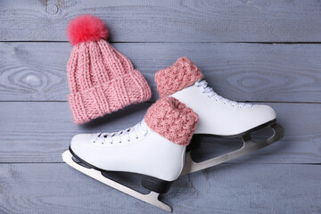 Wall Mural - Pair of ice skates and knitted hat on grey wooden background, flat lay