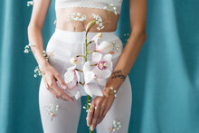 Cropped View Of Slim Woman In White Tights With Gypsophila Flowers Holding Orchid On Green Draped Background.