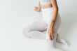 © LIGHTFIELD STUDIOS - partial view of tattooed woman in white tights with tiny flowers sitting on light grey.