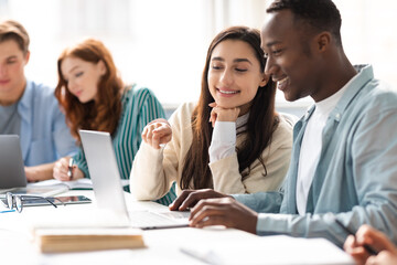 International smiling students sitting at desk working on group project