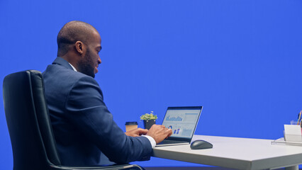 Wall Mural - Green Screen Office Background: Black Businessman Sitting at His Desk Working on a Laptop Computer. African American Man working with Data e-Commerce Analysis