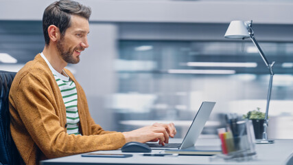 Poster - Modern Office: Handsome Businessman Sitting at His Desk Working on a Laptop Computer. Man working with Big Data e-Commerce Analysis. Motion Blur Background Showing Active Work Day.