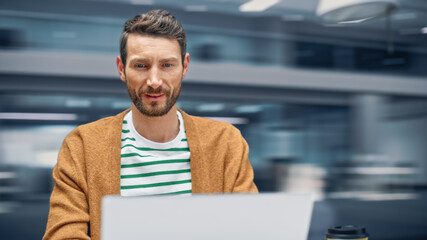 Leinwandbilder - Modern Office: Handsome Businessman Sitting at His Desk Working on a Laptop Computer. Man working with Big Data e-Commerce Analysis. Motion Blur Background Showing Active Work Day.