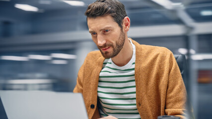 Poster - Modern Office: Handsome Businessman Sitting at His Desk Working on a Laptop Computer. Man working with Big Data e-Commerce Analysis. Motion Blur Background Showing Active Work Day.