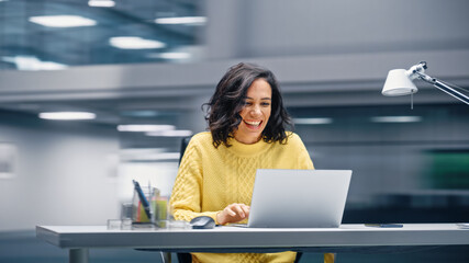 Poster - Modern Office: Happy Smiling Hispanic Businesswoman Sitting at Her Desk Working on a Laptop Computer Celebrates Victory. Latin Female Entrepreneur is a Happy Winner. Motion Blur Background