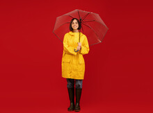 Autumn Style. Studio Shot Of Millennial Lady In Raincoat, Standing Under Umbrella And Posing Over Red Background