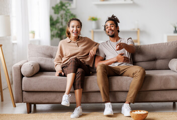 Wall Mural - Young overjoyed african american couple at home watching comedy movie, laughing out of loud