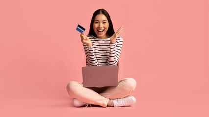 Online Payments. Cheerful young asian woman sitting with laptop and credit card