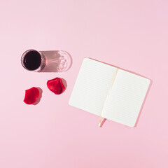 Wall Mural - Creative romance arrangement made of notebook, glass of drink and petals on a pink background. Minimal retro flat lay concept. Love and Valentine's Day inspiration. Copy space.