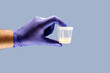 hand wearing nitrile glove holding semen or sperm sample collection container, semen donation concept