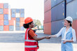 © Anatta_Tan - Caucasian female engineer and African worker, holding hand, are working in containers industry, logistic transport Import-Export Cargo, to business shipping and warehouse concept.