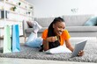 © Prostock-studio - Black lady lying on soft carpet with tablet pc and credit card, surrounded by gift bags, shopping in web store from home