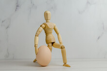 Wooden Man Holding Egg. Mannequin Got Down On Knee, Holding Egg. Concept Idea Presentation, Creative