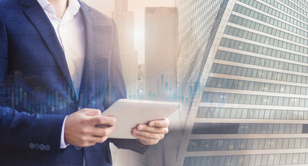 Poster - Double exposure of businessman using digital tablet overlaid with cityscape and candlesticks