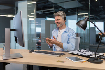 Wall Mural - Senior and experienced employee, advises the buyer on a video call, the man works in a modern office uses a headset for negotiations, and a webcam