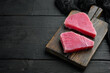 Pieces of raw tuna fish, on wooden cutting board, on black wooden background , with copyspace  and space for text