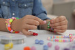 © New Africa - Little girl making beaded jewelry at table indoors, closeup
